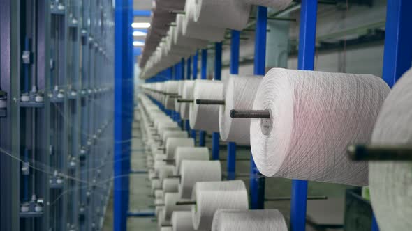 Textile Factory Equipment in Work. Bobbins with Threads Hang on a Metal Rack While Spooling.