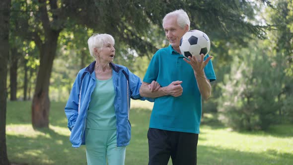 Front View Dolly Shot Happy Fit Senior Man and Woman Walking Arm in Arm with Soccer Ball Talking in