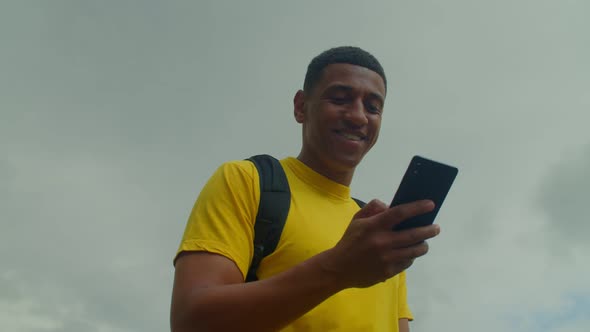 Portrait of Smiling Black Male Text Messaging Online on Cellphone on the Move