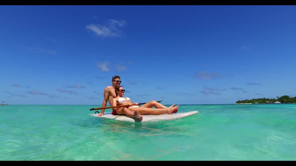 Man and lady sunbathing on tropical tourist beach wildlife by shallow ocean with white sand backgrou