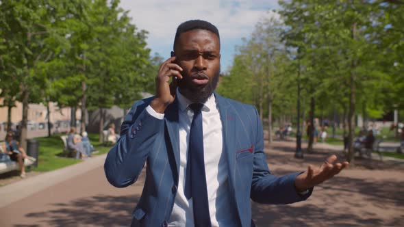 Young African Angry Businessman Talking on Phone with Difficult Client Walking Outdoors