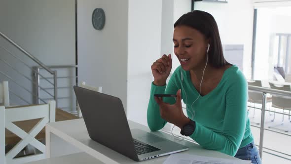 African american woman talking on smartphone and using laptop while working from home