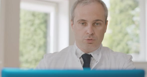 Close-up Portrait of Serious Doctor Offering Jar with Pills at Selfie Camera on Laptop, Confident