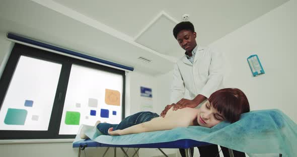 African American Physiotherapist Conducts Therapeutic Massage Therapy To a Young