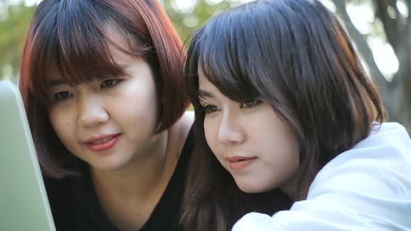 Young asian women lying on grass and using laptop and typing. Girls hands on keyboard.