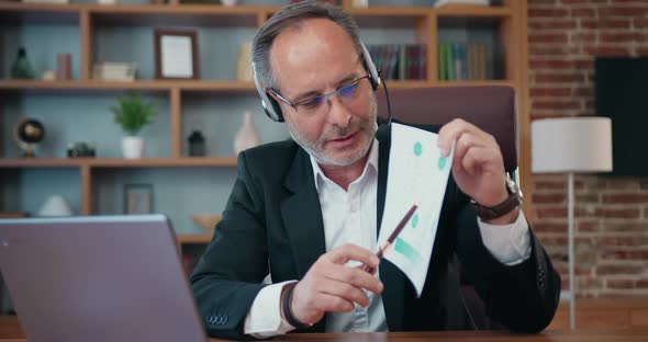 Businessman in Headphones with Mic Explaining Financial Chart to His Business Partners Via Videochat