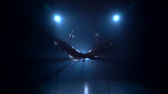 Two Female Balancer in Beige Leotard Back Lying Hang on Aerial Hoop on Black Background. Silhouette