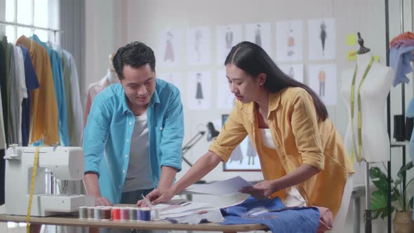 Asian Male And Female Designers Helping Each Other Rearrange The Papers While Designing Clothes