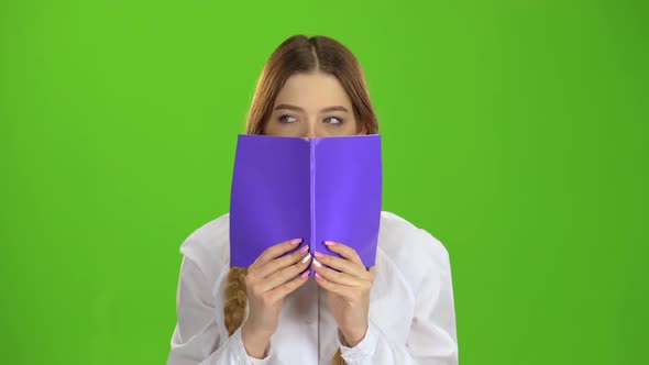 Schoolgirl Covered Her Face with a Notebook. Green Screen