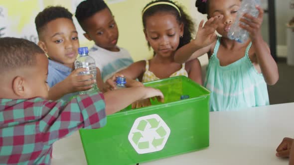 Video of happy african american pupils sorting plastic bottles for recycling in classroom