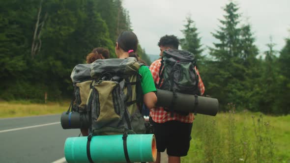 Positive Diverse Multiethnic Backpackers Walking Along Road on Mountain Hiking