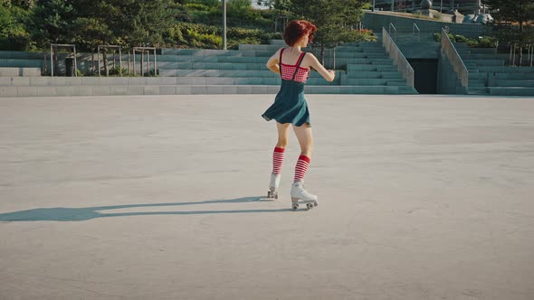 Young Gorgeous Woman Wearing Bright Pin Up Dress Rinking on Roller Skates in Urban Park Dancing and