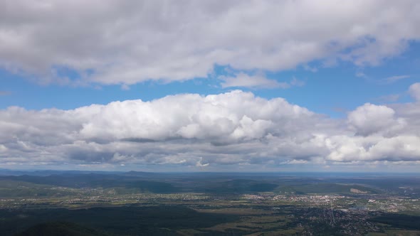Aerial View From High Altitude of Distant City Covered with Puffy Cumulus Clouds Flying By Before