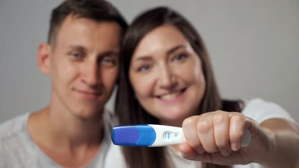 Closeup of Positive Pregnancy Test on Blurred Background of Happy Man and Woman