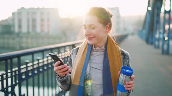 Caucasian Businesswoman in a Coat Walking Across the Bridge on a Frosty Morning Drinking Coffee and