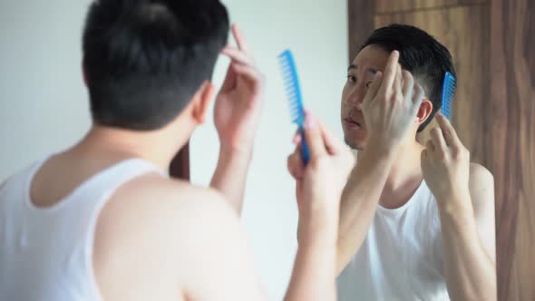 Young Male Brushing Hair While Looking in Mirror in Bathroom