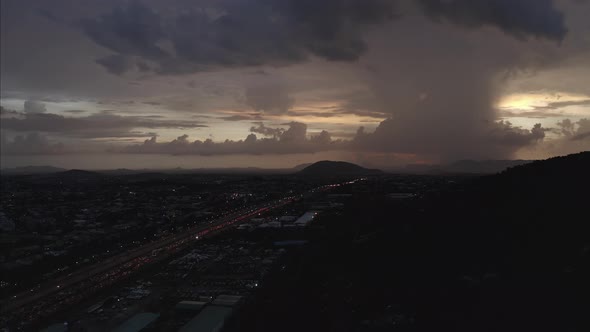 Aerial shot of a highway leading to a hill with a lightning strike on the horizon