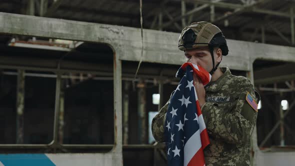 Male Soldier Kissing USA Flag in Destroyed Factory