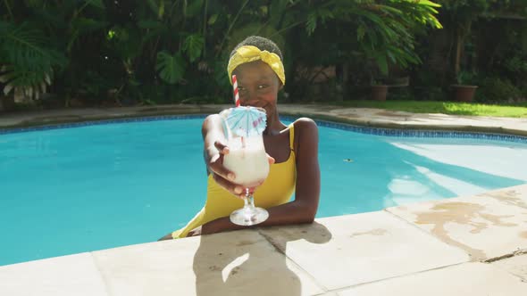 Portrait of happy african american woman standing in swimming pool making a toast with her drink