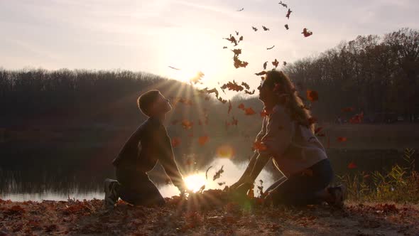 Woman with Leaf and Her Child Boy Making Leaves Fight in Autumn Yard.