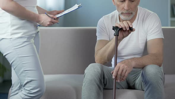 Caring female doctor filling clinical record, supporting male pensioner, clinic