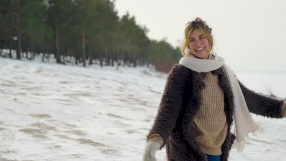 Woman playing in snowy winter woods while rejoicing with her arms open wide as she spinning