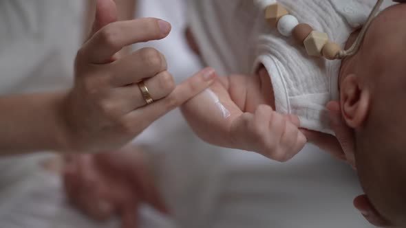Closeup Female Finger Rubbing Moisturizer in Hand of Newborn Baby in Slow Motion