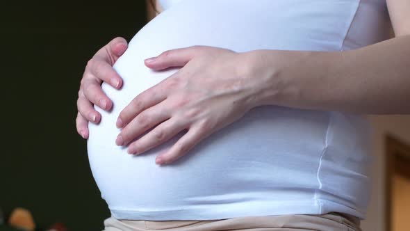 Pregnant girl in a white tank top is dancing.