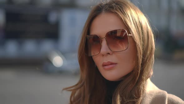 Beautiful Brunette Caucasian Woman in Sunglasses Looking at Camera Standing Outdoors on City Street