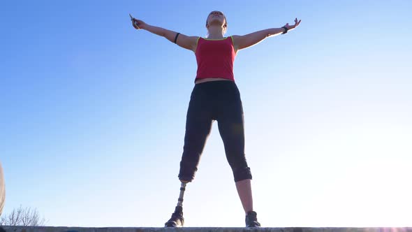 Sporty young woman with leg prosthesis raising arms