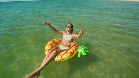 Happy Smiling Young Woman in Sunglasses Swimming on Inflatable Pineapple Floating Ring in Sea Water