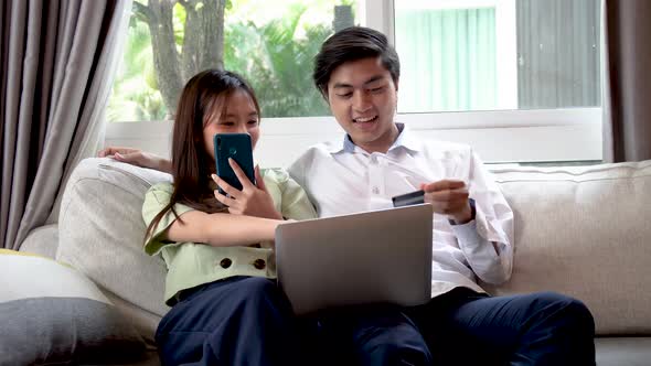 Happy asian couple using laptop for ecommerce doing online shopping together, watching video movie 