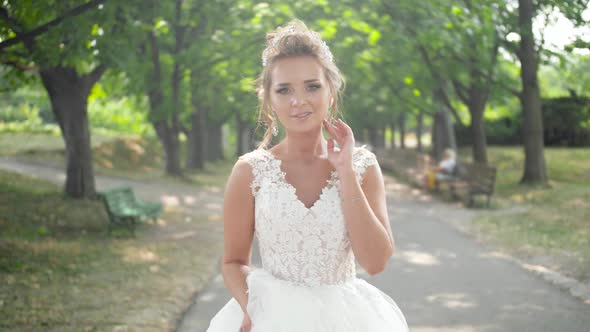  Portrait of Young Smiling Bride in Beautiful Bridal Dress Walking in Park Under Big Trees
