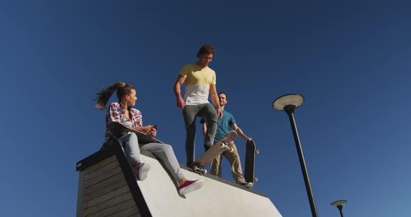 Happy caucasian woman and two male friends skateboarding on sunny day