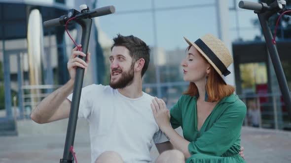Young Lovely Couple Sitting Talking and Having Fun with Electric Scooters