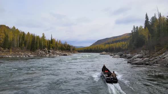 People in a Boat Pass the Rapids of a Stormy Mountain River Against the Backdrop of a Coniferous