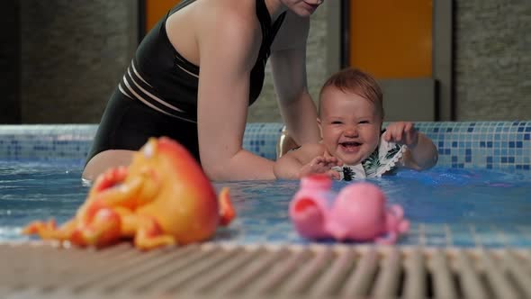 A Happy Little Baby Learns to Swim in the Pool with a Caring Mother