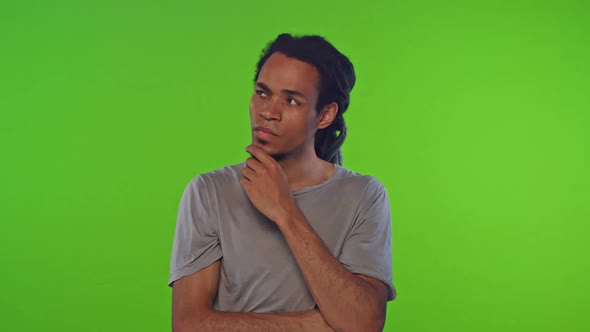 Young African American Man Thinks and Touches Chin Stands in Green Studio