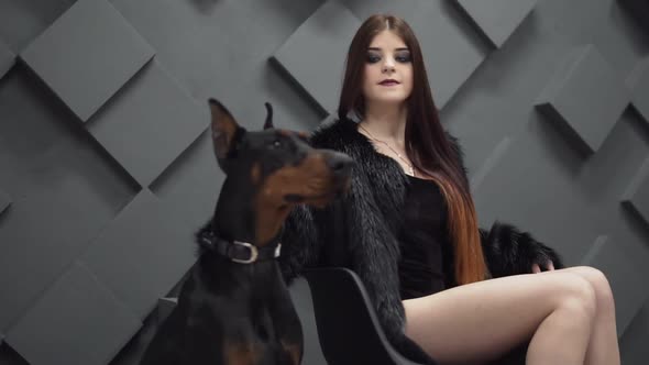 Sexy Girl with Long Hair in Black Fur Coat Sitting Near Dog in Studio