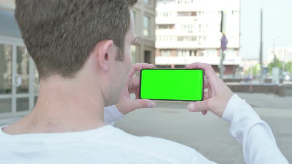 Young Man Holding Horizontal Smartphone with Green Screen Outdoor