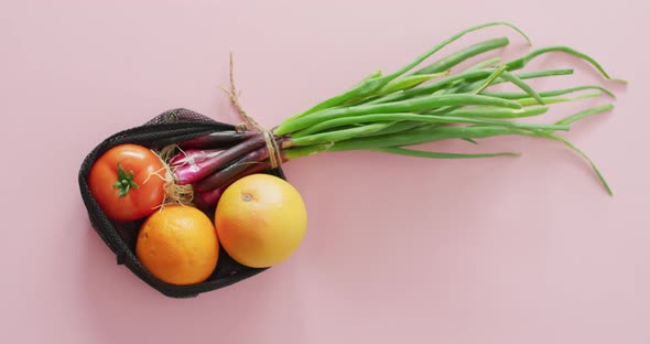 Video of fresh fruit and vegetables in black bag over pink background