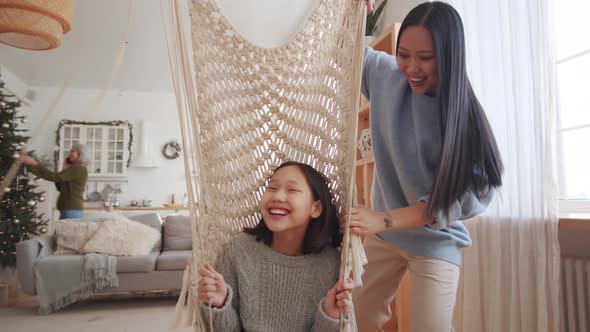 Joyous Asian Girl Swinging on Indoor Swing with Help of Loving Mom