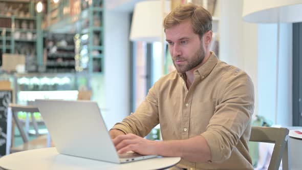 Laptop Use By Young Man Smiling at Camera in Cafe