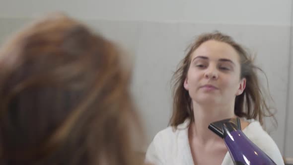 Portrait of Lovely Young Caucasian Woman Looking at the Camera and Dancing While Drying Her Hair