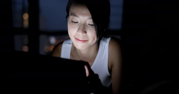 Woman using cellphone and lying on bed at night 