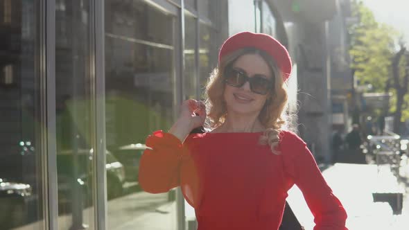 Luxurious Young Blonde Woman Stands on the Street in the City and with a Smile Throws a Jacket Over