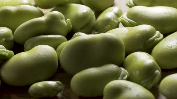 Slider shot at extreme close up of a pile of sweating, backlit, green fava beans piled on top of a c