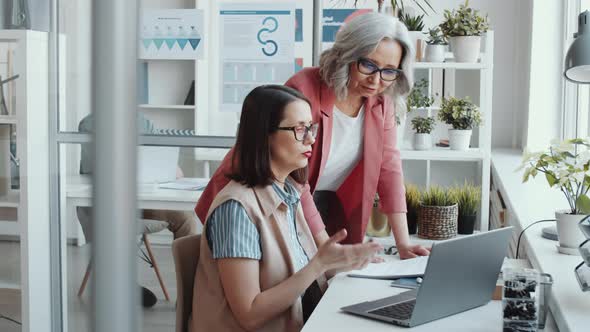Senior Female Manager Helping Young Woman with Project on Laptop