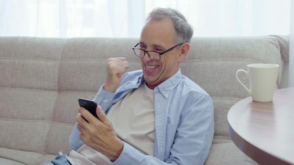 Elderly Man Rejoices Looking Into Smartphone