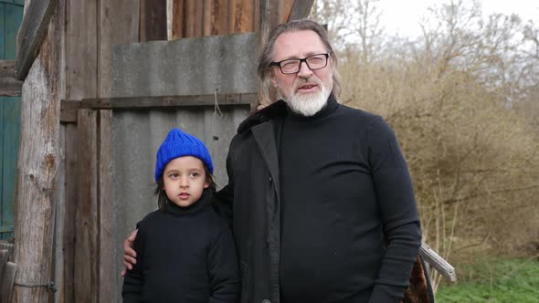 Grandson a Child in a Blue Knitted Hat Stands with His Grandfather